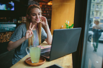 Young blonde in a cafe works with a laptop. She talks on Skype. On the table is a cup of green tea.