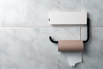Finished roll of toilet paper hanging from a metal dispenser in a tiled bathroom