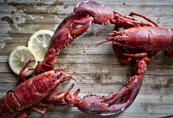 Steamed red lobsters with lemon, seafood utensils on the rustic wooden table. Maine lobsters. Two boiled lobsters.