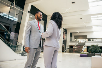Happy successful business colleagues greeting each other. Diverse business man and woman standing in office hall, shaking hands, talking, smiling. Congratulation concept