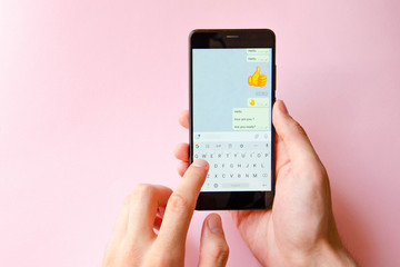 A male hand holds a smartphone, points a finger, types. Communication on a smartphone, correspondence. Place for text. Smartphone in hand on a pink  background.