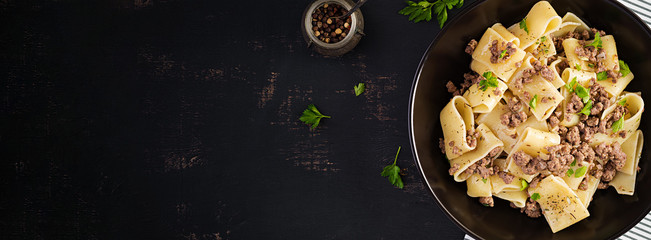 Pasta Calamarata with minced meat in black bowl. Italian cuisine. Top view, overhead, banner