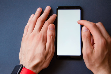 A male hand holds a smartphone, points a finger, types. Communication on a smartphone, correspondence. Place for text. Smartphone in hand on a gray  background.