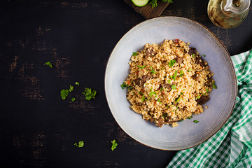Bulgur pilaf with meat and and vegetables. Delicious healthy warm lunch on black background. Eastern cuisine. Top view, overhead, flat lay