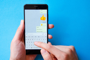 A male hand holds a smartphone, points a finger, types. Communication on a smartphone, correspondence. Place for text. Smartphone in hand on a blue  background.