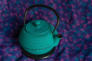 Turquoise cast iron teapot on purple background