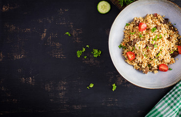 Bulgur pilaf with meat and and vegetables. Delicious healthy warm lunch on black background. Eastern cuisine. Top view, overhead, flat lay