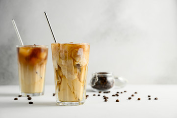 Two glasses of iced coffee on a light concrete table. Frozen swirls of milk. Horizontal orientation, copy space.