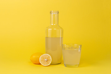 Bottle with lemon juice and a glass next to it and whole and sliced lemons isolated on a yellow background