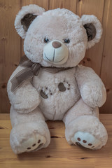 light brown teddy bear sitting on wooden floor against background of wooden walls