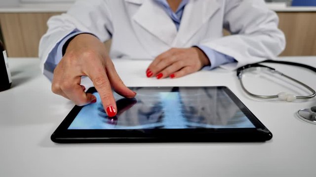 female doctor working in office checks chest xrays on tablet dolly shot