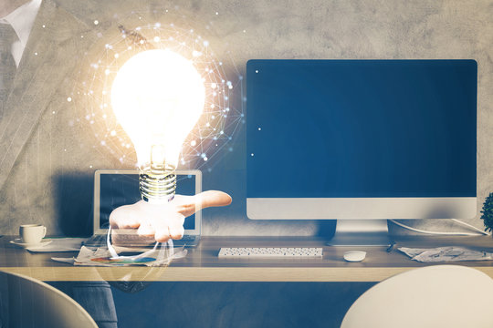 Computer on desktop in office with bulb icon hologram. Multi exposure. Concept of idea.