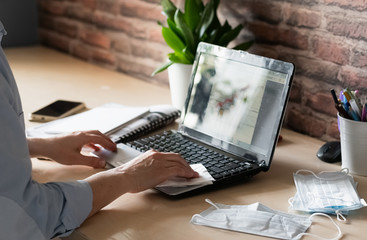 A female hand wipes a laptop with a wet alcohol wipe to prevent infection with coronovirus flu....