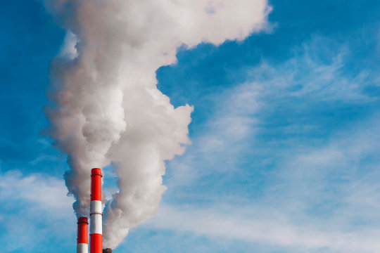 Environmental pollution, environmental problem, smoke from the chimney of an industrial plant or thermal power plant on a background of blue sky with clouds