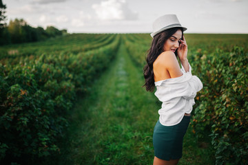 Beautiful romantic young girl in light peasant dress and a hat enjoying a walk around the tea...