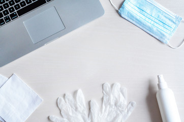 flat lay remote work kit on wooden office desk with hand sanitizer, face mask, gloves,  solution against the spread of coronavirus for quarantined employees. sanitization of the home workplace