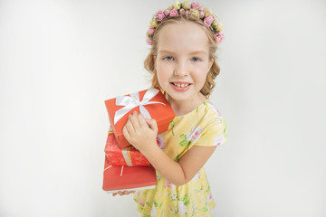 Little girl smiling at camera with beautiful decoration on her head made of flowers and holding gift boxes in her hands