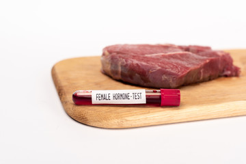 Selective focus of test tube with female hormone test on chopping board with raw meat isolated on white