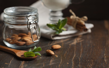 almonds in a small glass jar close up and a glass of milk on a dark background