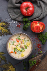 Finnish soup with salmon, potatoes, carrots, tomatoes and cream in a deep gey bowl. Parsley, tomatoes, knife, spices  and salt on a grey background. Top view. Background image, copy space