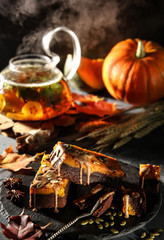 Fototapeta na wymiar Chocolate pumpkin dessert. Brownie with chocolate sauce and pumpkin seeds on a black board. Teapot with tea leaves, mint and quince. The smoke from the tea. Autumn atmosphere. Sunny day