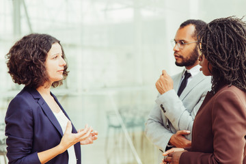 Focused mux raced colleagues discussing project. Business man and women standing at outdoor glass wall, talking to each other. Cooperation concept