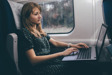 Young woman travel in train. Remote work on laptop during sitting inside. Student or tourist have small trip. Business. Typing on keyboard.