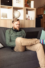 Young man with laptop sitting on sofa at living room. Working in informal environment, remote work, home office, freelancer, self isolation concept