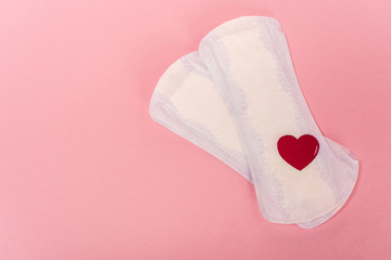 Top view of feminine pads with paper heart on pink background