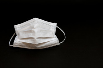 White surgical mask for protection against Coronavirus COVID-19 (SARS-CoV-2) and other contagious diseases. Copy space. Horizontal shot. Isolated on black background.