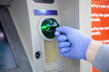 male hand in disposable protective glove uses card at ATM