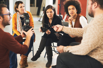 Multicultural group of attendees listening to tutor talking about camera parts.