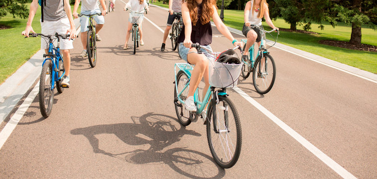 People riding bicycles in city park on asphalt road. Gealthy lifestyle and health care. Cut view of five people hacing fun together on road. Beautiful sunny day outside.