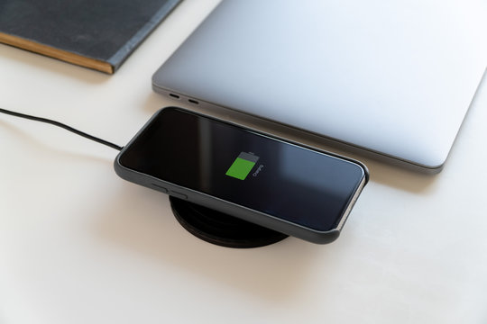 Wireless Charging Concept. A phone charging next to the laptop in the minimalist workspace 