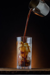 Iced coffee wWIth fresh arabica espresso. FResh milk and coffee splashing into a glass filled with ice. Barista coffee with dark background