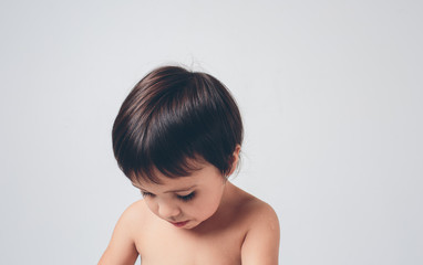 sad, disoriented child looks down on a white background. The gill or boy has brown hair and skin