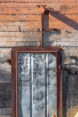 Natural texture of a beige cement wall and an iron rusty door aged by time with scuffs and moss in...