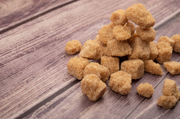 Pieces of brown cane sugar in a pile on a wooden background. Close up.