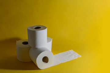 A stack of four white disposable toilet rolls on a bright yellow background. One roll lies untwisted. Soft fresh cotton. Essential goods. Purchasing power. Copy space. Drops a shadow from an object.