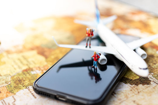 Miniature people: travelers with backpack standing on mobile phone travel by plane and booking ticket online. Image use for travel business concept.