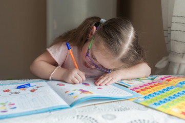 Happy pretty child girls sitting at the table and writes. Educational activities at home. Distance learning. Girl with glasses. Vision problems