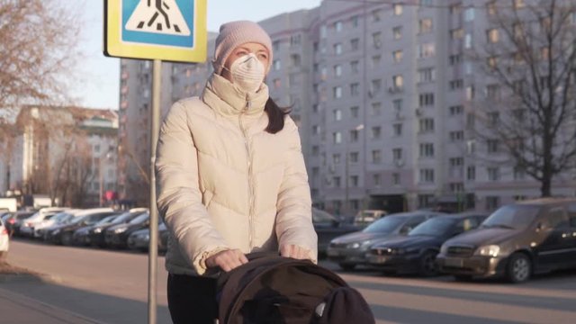 A woman in a medical mask walks with a child in a stroller on the street
