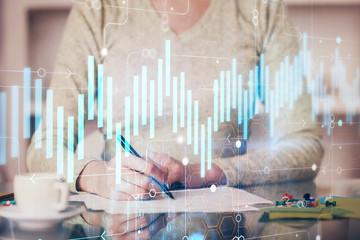 Hand taking notes in notepad. Forex chart holograms in front. Concept of research. Double exposure