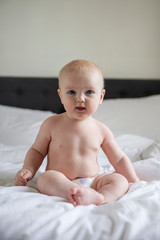 Cute baby wearing a nappy sat on a bed looking at the camera