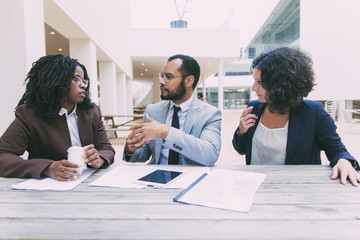 Multiethnic business colleagues discussing documents in cafe. Business man and women sitting at...