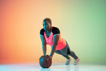 Young african-american plus size female model's training on gradient background in neon light....