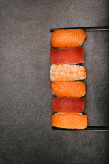 Stock photo of nigiri sushi stacked on the side between two chopsticks, on a black background.