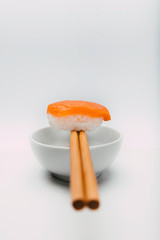 Stock photo of salmon nigiri sushi balanced on two chopsticks in a bowl of soy sauce. All on white background.
