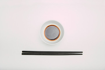 Stock photo of soy bowl with black chopsticks underneath on a white background.