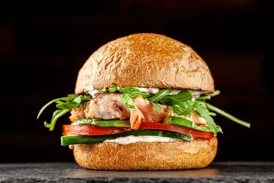 Vegetarian American Cuisine. Burger with red fish salmon, arugula, cucumbers and tomatoes, white sauce. Burger on a black background. background image, copy space text